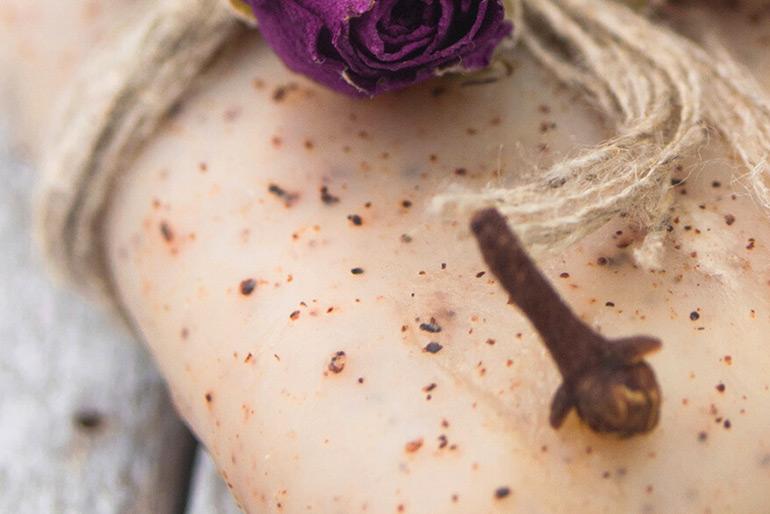 The cinnamon soap bar with twine wrapped around it and a singular bit of clove sitting on top of the bar, a rose can be seen behind the clove.
